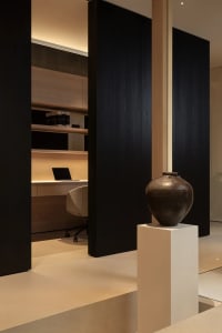 A modern office space with a wooden floor, black walls, a desk, chair, and a vase on a pedestal