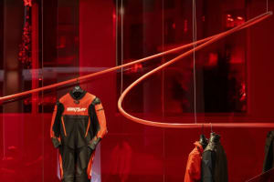 A red room with a circular light and mannequin displaying a black and orange wetsuit, surrounded by other clothing items in a visually appealing retail display