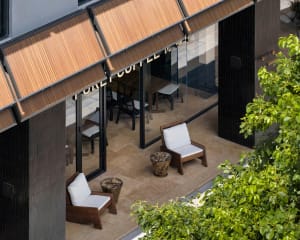 Cozy coffee shop with a brown wooden exterior, featuring a variety of seating options, potted plants, and a welcoming atmosphere