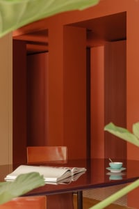 A warm and inviting dining space with a red wall, a wooden table, and a potted plant, set with a cup, a bowl, and a spoon