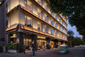A well-lit coffee shop with a glass front, natural light, and comfortable seating, surrounded by a hotel building