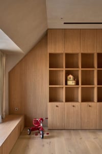 A dimly lit room with wooden walls and floor, featuring a wooden bookshelf with a toy house and a red toy car, creating a cozy and intimate atmosphere