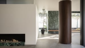 A modern living room with a predominantly white color scheme, a stone wall, a fireplace, and a potted plant, well-lit by natural light through the windows