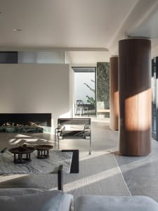 Cozy living room with a fireplace, couch, chair, and dining table, decorated with vases, bowls, and potted plants, and featuring wood, stone, and glass materials in a well-lit space with natural light