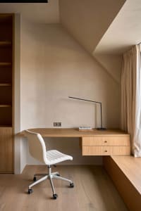 A home office with a wooden desk, a white chair, and natural light from an open window