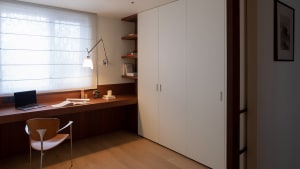 A cozy bedroom with a wooden floor, a white cabinet, a bed, a chair, a desk, and a book, creating a warm and inviting atmosphere