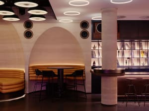 A well-lit restaurant interior with a bar, dining area, and modern decor, featuring a variety of books on the walls