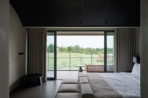 A well-lit living room with a couch, chair, and dining table, featuring a large window with a view of the outdoors and a mix of wood and metal materials
