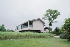 A modern house with a white exterior, surrounded by a lush green field, featuring a large window and several smaller windows, with natural light streaming in