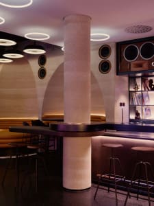 A modern bar with a mix of wood and metal materials, featuring a counter, pillar, and comfortable seating for guests
