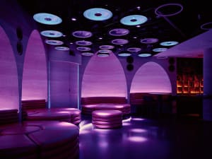 Purple-lit lounge with a futuristic design, featuring a circular shape and a dome-like ceiling, with couches and chairs throughout