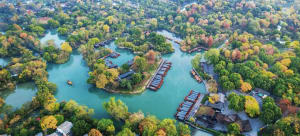 A modern house surrounded by trees and a river, with boats on the water and sunlight streaming through the trees