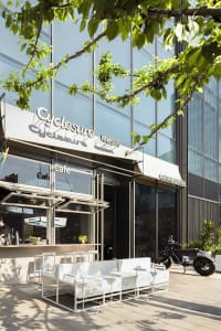 A modern cafe with a white facade, a motorcycle parked outside, and natural light pouring in through the windows