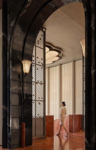 A woman walks down a hallway with marble flooring, surrounded by elegant decorations and dark tones