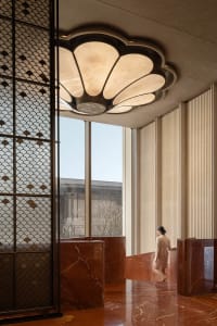 Well-lit lobby with a marble floor, marble wall, and marble ceiling, featuring a bench and a woman walking towards the camera