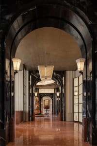 A grand lobby with a high ceiling, marble-like walls, decorative elements, and a large archway leading to a doorway