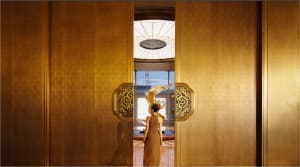 A woman walks through a doorway in a luxurious gold-colored interior with a decorative dragon design on the doorframe