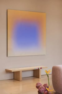A cozy living space with a modern art painting on the wall, a wooden bench, and a chair, in a yellow and blue color scheme