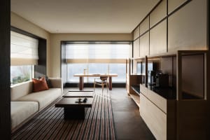 A well-lit modern living room with a couch, coffee table, dining table, and kitchen area, featuring wood furniture and a focus on functionality and comfort