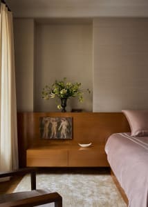 A well-lit bedroom with a bed on the right, a bench on the left, and a vase with flowers on the bench