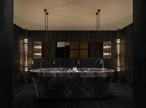 A dimly lit modern bathroom with a large marble bathtub, sink, and mirror