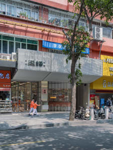 A street scene with a mix of modern and traditional buildings, lined with trees and featuring motorcycles, in warm earth tones with natural sunlight