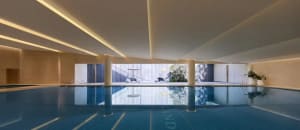 A relaxing pool area with a hotel building in the background, surrounded by a deck and chairs, inviting guests to unwind