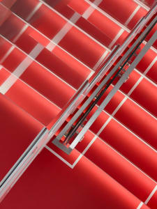 A staircase with red railings in a room with a red wall, surrounded by natural light from a window