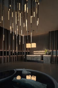A well-lit modern living room with a chandelier, stone and wood walls, a couch, and a dining table