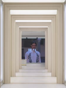 A modern hallway with a white color scheme and a man on a screen in the background