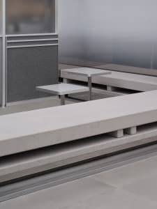 Dining area with a concrete bench and metal table in a well-lit room with a glass wall and cement floor