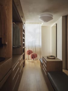 Cozy modern bedroom with a wooden floor, white wall, and dim lighting, featuring a bench and two pink feathered objects