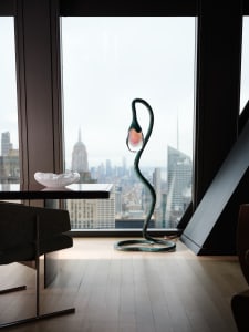 A modern living room with a large window showcasing a cityscape view, featuring a dining table, chair, couch, potted plant, and various decorative items, with natural light creating a bright and inviting space