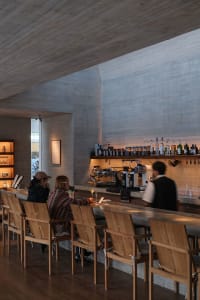 A modern bar with a counter and chairs, featuring bottles and cups, creating an inviting atmosphere for socializing and enjoying drinks