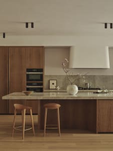 Modern kitchen with wooden cabinets, marble countertop, sink, oven, microwave, and decorative vase