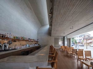 Industrial-style bar with a concrete counter, wooden chairs, and natural light from windows