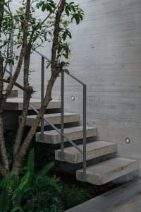 A concrete staircase with a metal railing and a potted tree growing in front of it, set in an outdoor urban scene