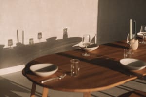 A dining room table set with wine glasses, bowls, and cups, surrounded by chairs and a vase, in a warm and inviting atmosphere
