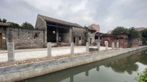 A rustic building with a brick facade and stone-like texture, situated next to a body of water with a boat in the distance, creating a serene atmosphere