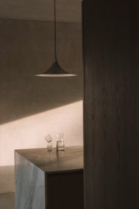 Dining area with a wooden table, wooden floor, and a hanging light fixture, set with glasses and a cup, in a warm and cozy atmosphere
