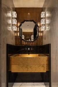 Modern bathroom with a gold-toned sink, mirror, and drawer, set against a black countertop, in a well-lit space with a warm and inviting atmosphere