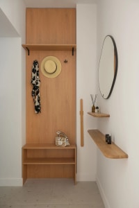 A cozy bedroom with a wooden shelf and mirror, featuring a bed in the background and various personal items on the shelf
