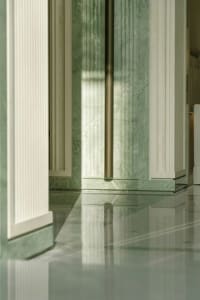 Green marble walls and floor in a dimly lit hallway with white columns