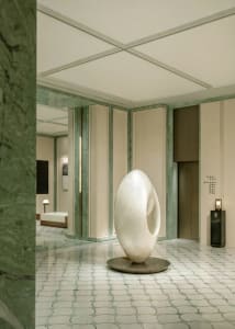 A large white sculpture on a pedestal in a dimly lit room with a marble floor, surrounded by a contemporary art gallery setting