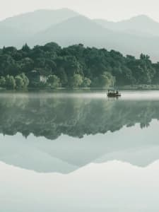 A serene lakefront house with a boat floating in the water, surrounded by trees