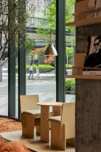 A modern restaurant with a wooden table and glass top, two chairs, and a large window allowing natural light to enter, creating an inviting and comfortable atmosphere for guests