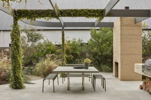 A well-lit outdoor patio with a dining table, chairs, and a vase with flowers, surrounded by a stone wall and a fireplace in a garden setting