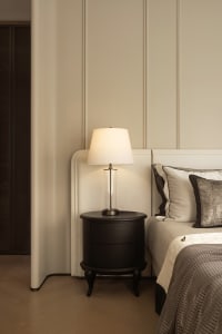 A white bedroom with a bed, nightstand, and lamp, featuring a clean and bright appearance with natural light and a minimalist aesthetic
