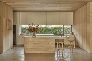 A well-lit kitchen with a marble countertop, wooden cabinets, a sink, refrigerator, and stools, creating a bright and inviting atmosphere