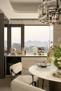 A modern kitchen with white cabinets, a marble countertop, a dining table, and chairs, surrounded by natural light from a large window